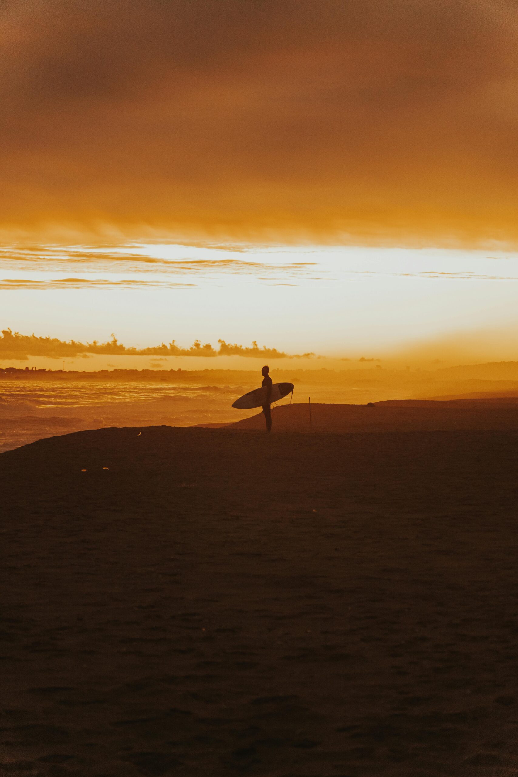 A silhouetted surfer stands on Punta del Este beach against a dramatic sunset sky.